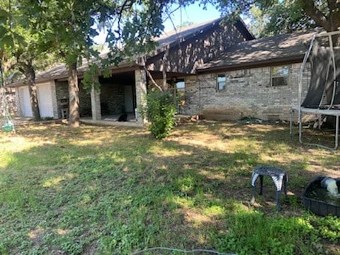 back of house featuring a trampoline and a yard