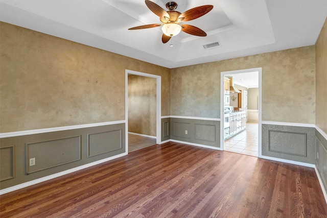 spare room featuring a raised ceiling, wood-type flooring, and ceiling fan