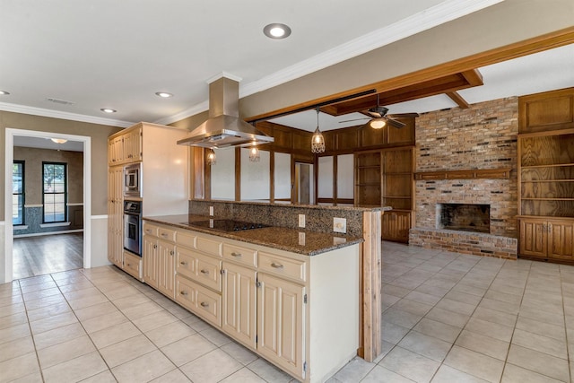 kitchen with appliances with stainless steel finishes, island range hood, dark stone counters, light tile patterned floors, and a brick fireplace