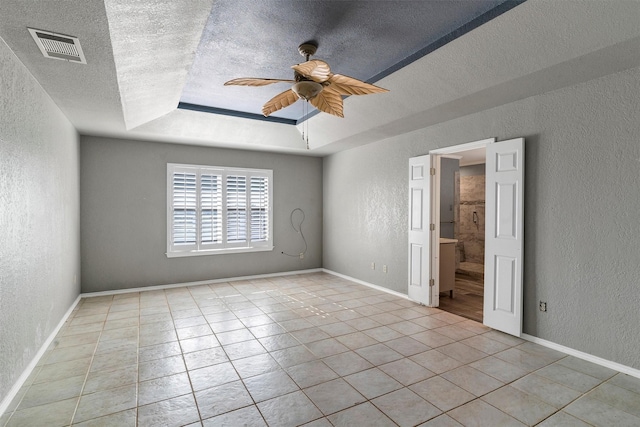 tiled spare room featuring ceiling fan, a tray ceiling, and a textured ceiling