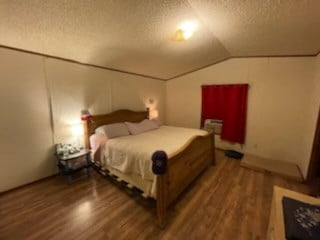 bedroom featuring hardwood / wood-style flooring, vaulted ceiling, and a textured ceiling