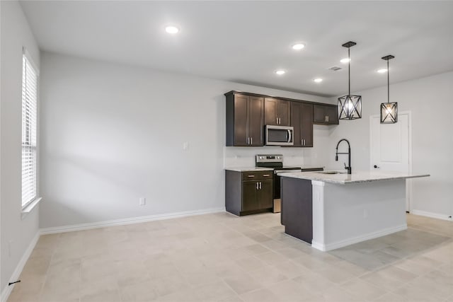 kitchen with light stone counters, plenty of natural light, stainless steel appliances, sink, and an island with sink