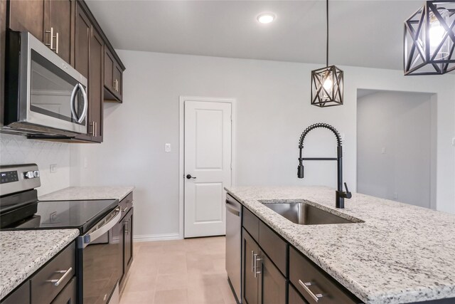 kitchen featuring light stone countertops, a center island with sink, pendant lighting, appliances with stainless steel finishes, and dark brown cabinetry