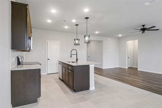 kitchen with light hardwood / wood-style flooring, sink, ceiling fan, hanging light fixtures, and a center island with sink