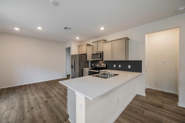 kitchen with stainless steel appliances, hardwood / wood-style floors, sink, kitchen peninsula, and decorative backsplash