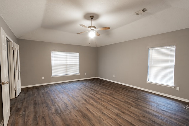 unfurnished room featuring dark wood-type flooring, ceiling fan, a raised ceiling, and a wealth of natural light