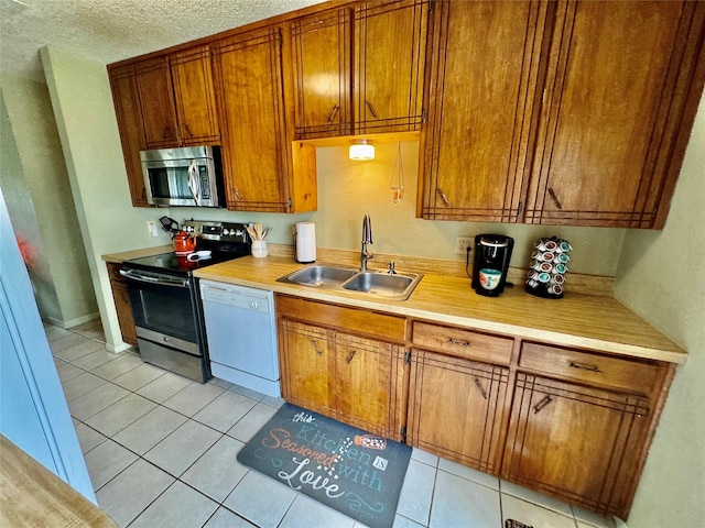 4506 Azalea Dr, Granbury, TX 76049 - kitchen with appliances with stainless steel finishes, a sink, light tile patterned flooring, brown cabinets, and light countertops