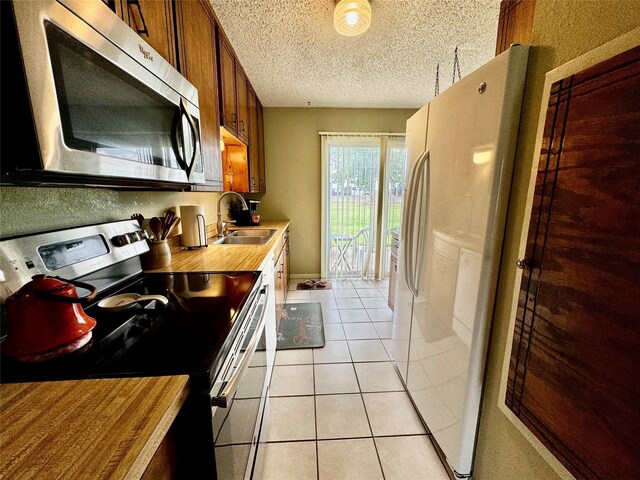 kitchen with sink, appliances with stainless steel finishes, a textured ceiling, and light tile patterned flooring