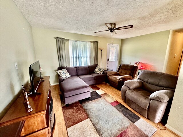 living room featuring ceiling fan, a textured ceiling, and light wood-type flooring