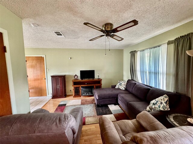 living room featuring light hardwood / wood-style floors, a textured ceiling, and ceiling fan