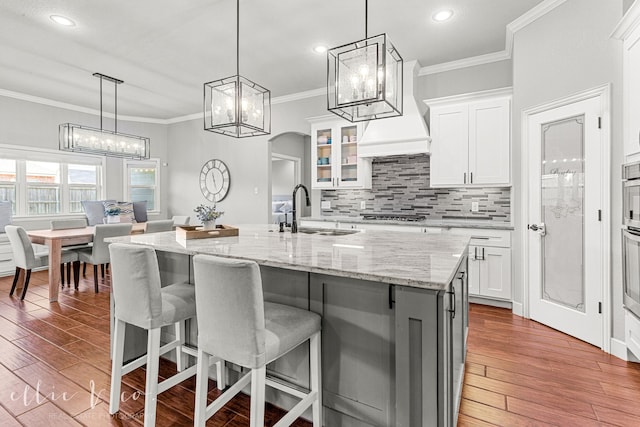 kitchen with white cabinetry, light hardwood / wood-style flooring, an island with sink, a kitchen breakfast bar, and sink