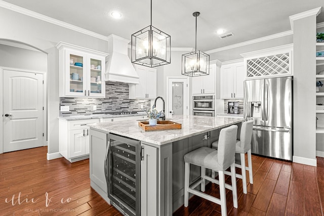 kitchen featuring custom exhaust hood, beverage cooler, stainless steel appliances, dark hardwood / wood-style flooring, and a kitchen island with sink