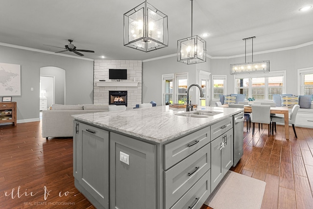 kitchen with a stone fireplace, sink, a kitchen island with sink, ceiling fan with notable chandelier, and hardwood / wood-style flooring