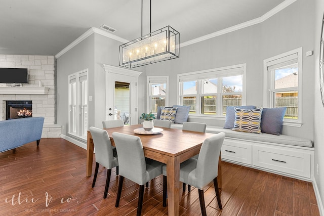 dining area featuring a wealth of natural light, a stone fireplace, dark hardwood / wood-style floors, and crown molding