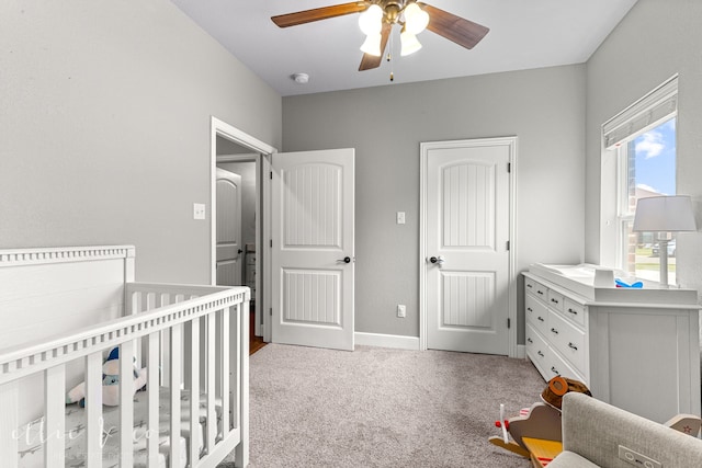 bedroom featuring a crib, light colored carpet, and ceiling fan