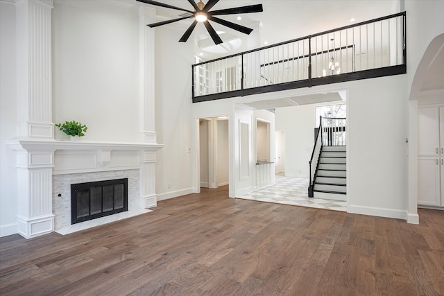 unfurnished living room with a stone fireplace, ceiling fan, hardwood / wood-style floors, and a towering ceiling