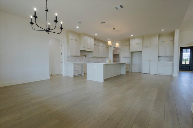 kitchen with white cabinetry, a large island, decorative backsplash, decorative light fixtures, and a notable chandelier