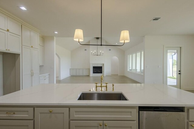 kitchen featuring an island with sink, lofted ceiling, hanging light fixtures, light stone counters, and sink