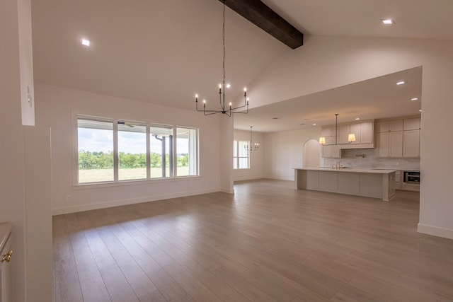 unfurnished living room featuring light wood-type flooring, a chandelier, beam ceiling, and high vaulted ceiling