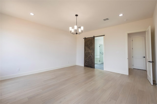 empty room featuring an inviting chandelier, light hardwood / wood-style flooring, and a barn door