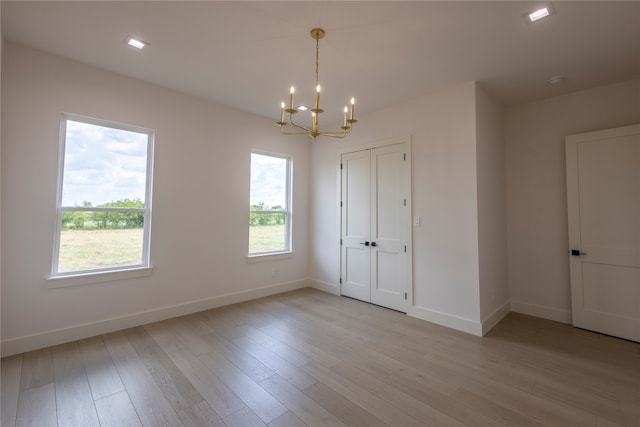 spare room featuring light wood-type flooring and an inviting chandelier