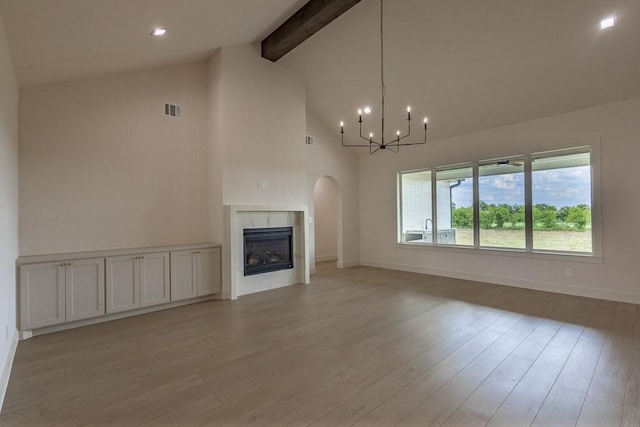 unfurnished living room with a tile fireplace, an inviting chandelier, beam ceiling, and light hardwood / wood-style flooring