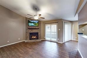 unfurnished living room featuring dark hardwood / wood-style floors, a fireplace, brick wall, and ceiling fan