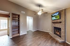 unfurnished living room with hardwood / wood-style floors, built in shelves, a brick fireplace, brick wall, and ceiling fan