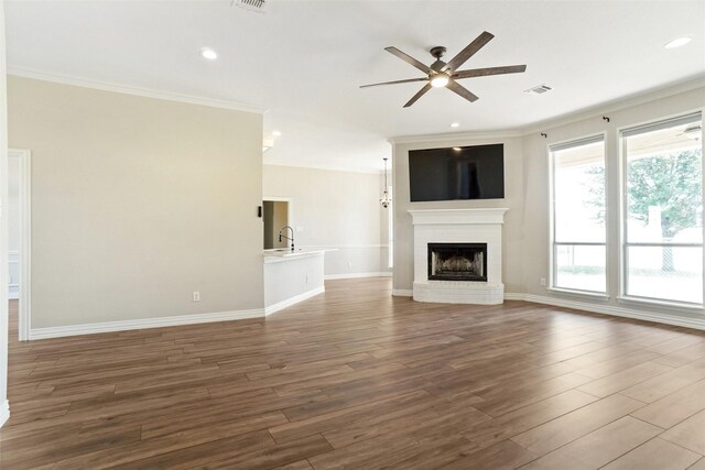 unfurnished living room with ornamental molding, a brick fireplace, ceiling fan, and hardwood / wood-style floors