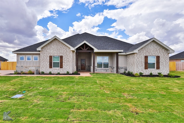 view of front facade featuring a shingled roof, brick siding, fence, a front lawn, and board and batten siding