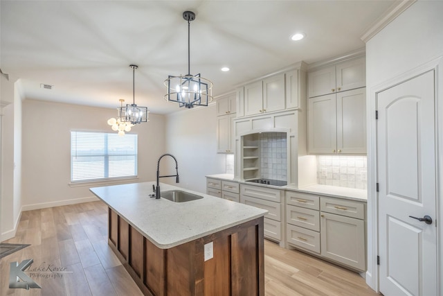 kitchen featuring light wood finished floors, tasteful backsplash, hanging light fixtures, a kitchen island with sink, and a sink