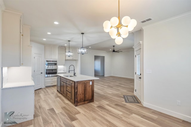 kitchen with an island with sink, decorative light fixtures, light countertops, crown molding, and a sink