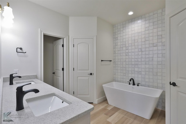 bathroom featuring tile walls, double vanity, a freestanding bath, a sink, and wood finished floors