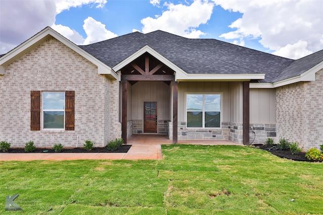 view of front facade featuring board and batten siding, a front yard, brick siding, and a shingled roof