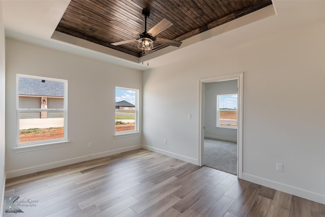 unfurnished room with baseboards, a raised ceiling, a ceiling fan, wood ceiling, and light wood-style floors