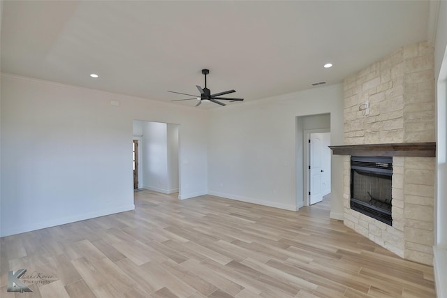 unfurnished living room with light wood finished floors, ceiling fan, crown molding, and a stone fireplace