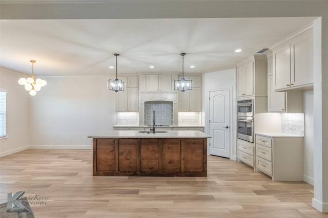 kitchen with an island with sink, a chandelier, light countertops, and pendant lighting