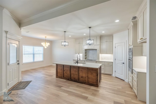 kitchen featuring a notable chandelier, a sink, light countertops, an island with sink, and decorative light fixtures