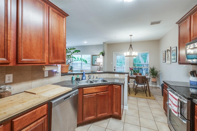 kitchen featuring pendant lighting, sink, light tile patterned floors, appliances with stainless steel finishes, and a chandelier