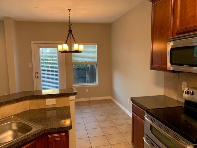 kitchen featuring stainless steel appliances, a notable chandelier, dark stone countertops, hanging light fixtures, and light tile patterned flooring