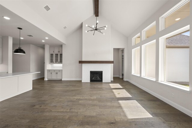 unfurnished living room with a fireplace, dark wood-type flooring, a chandelier, and beamed ceiling