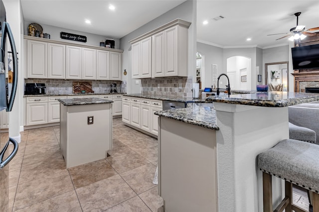 kitchen with a center island, open floor plan, dark stone countertops, a peninsula, and black fridge