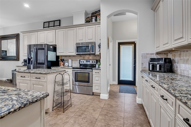 kitchen with arched walkways, light tile patterned floors, stainless steel appliances, visible vents, and light stone countertops