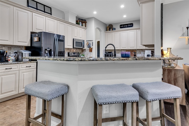 kitchen featuring light tile patterned floors, stone countertops, black fridge with ice dispenser, a kitchen breakfast bar, and stainless steel microwave