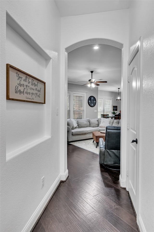 hall featuring arched walkways, dark wood-style floors, and baseboards