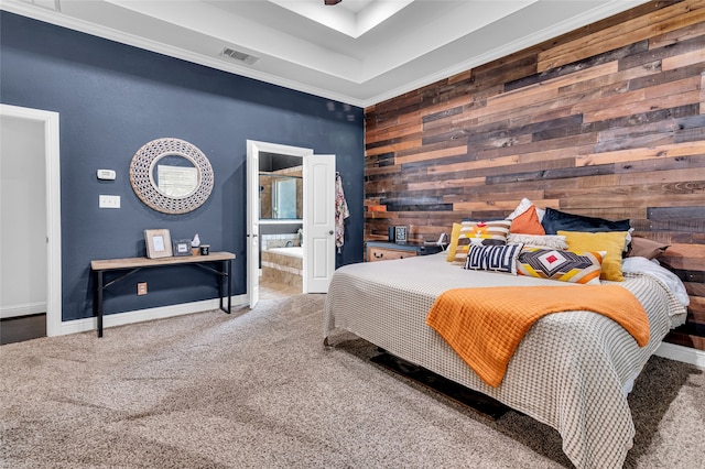 carpeted bedroom with an accent wall, wood walls, visible vents, baseboards, and ensuite bath