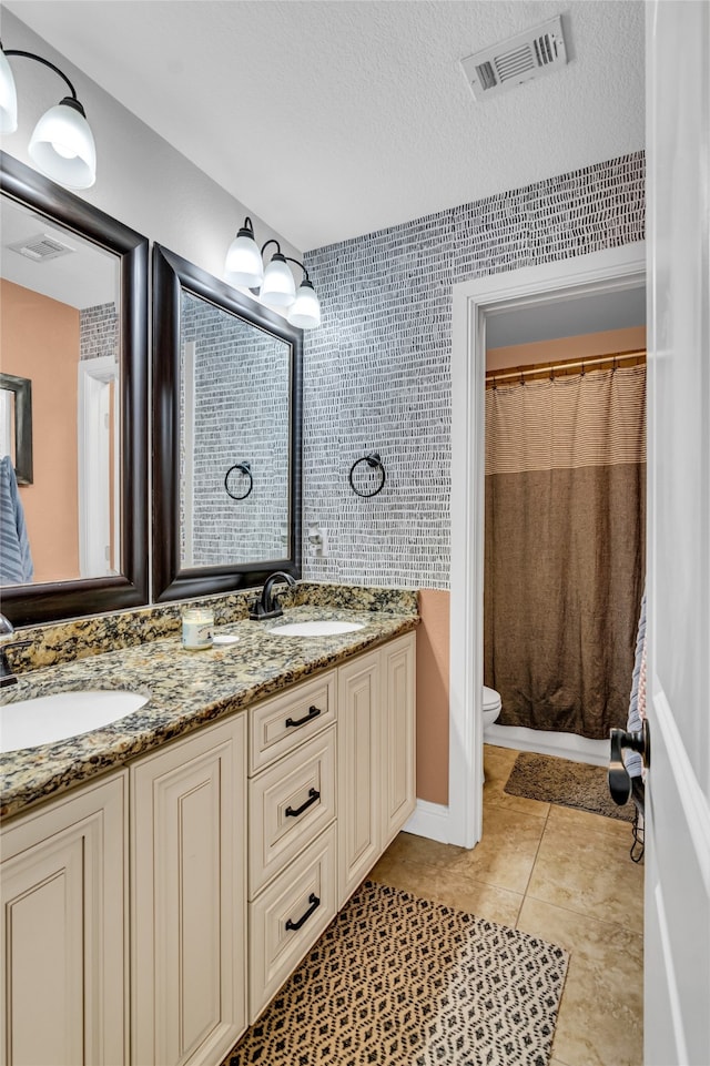 full bathroom with toilet, double vanity, visible vents, and a sink