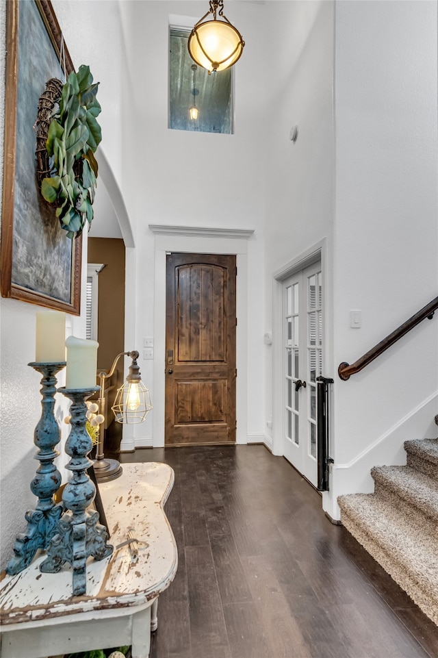 foyer with arched walkways, dark wood-type flooring, stairway, and a towering ceiling