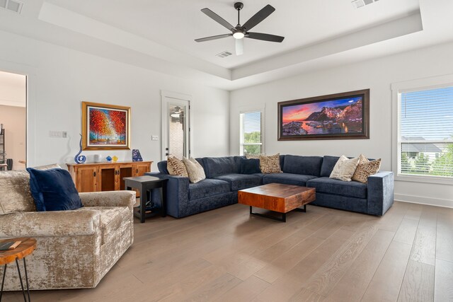 living room with ceiling fan, a tray ceiling, and light hardwood / wood-style flooring