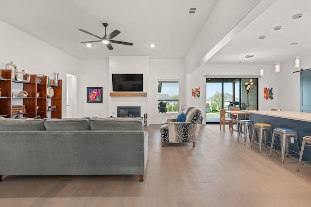 living room featuring light wood-type flooring, ceiling fan, a fireplace, and a barn door